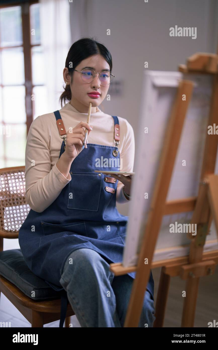 Jeune artiste féminine asiatique tenir le pinceau tout en regardant sur la toile à penser l'idée peinture art. Banque D'Images