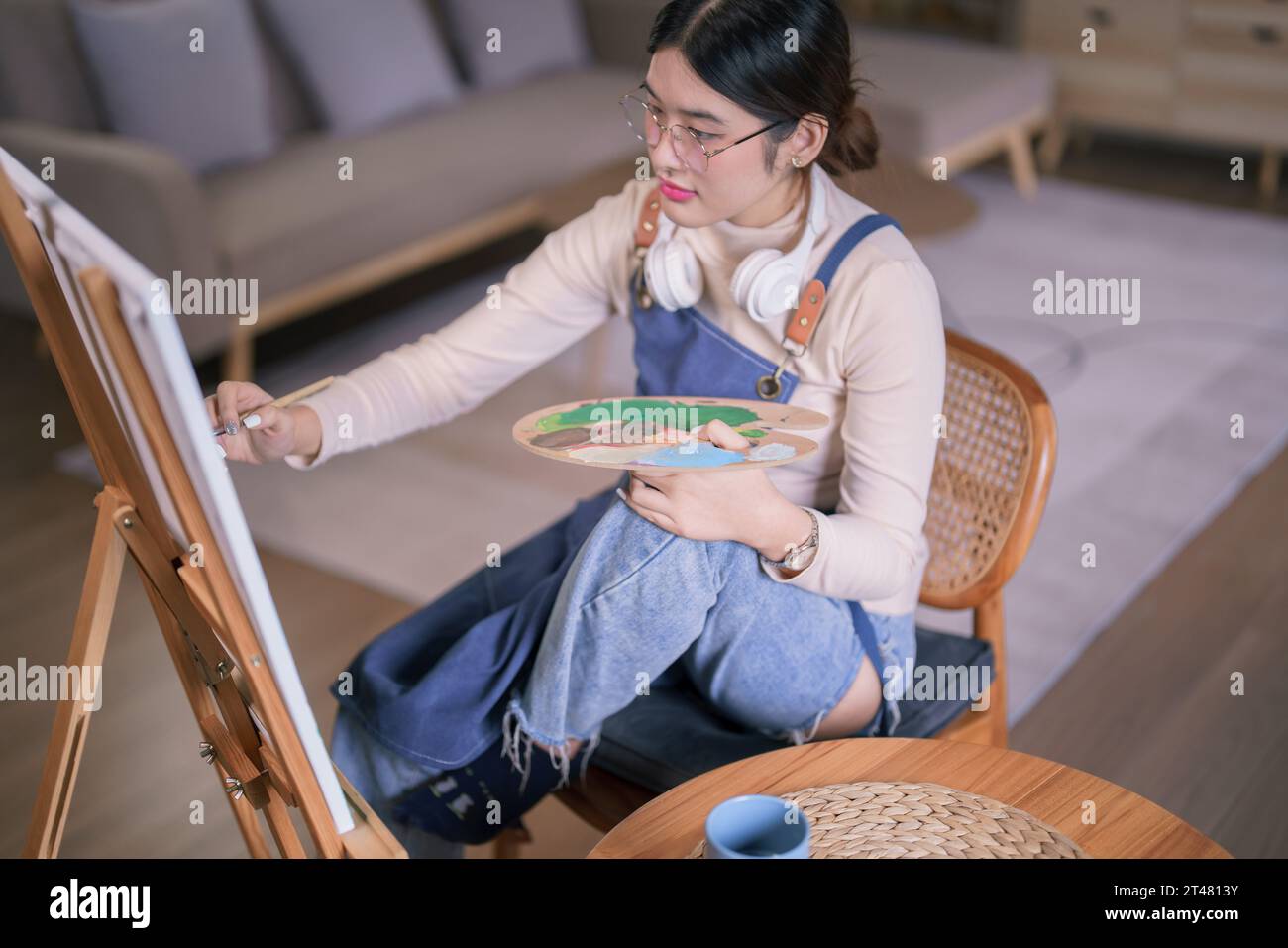 Jeune artiste féminine asiatique porter un casque dans son cou et utiliser des œuvres d'art de peinture au pinceau sur toile. Banque D'Images