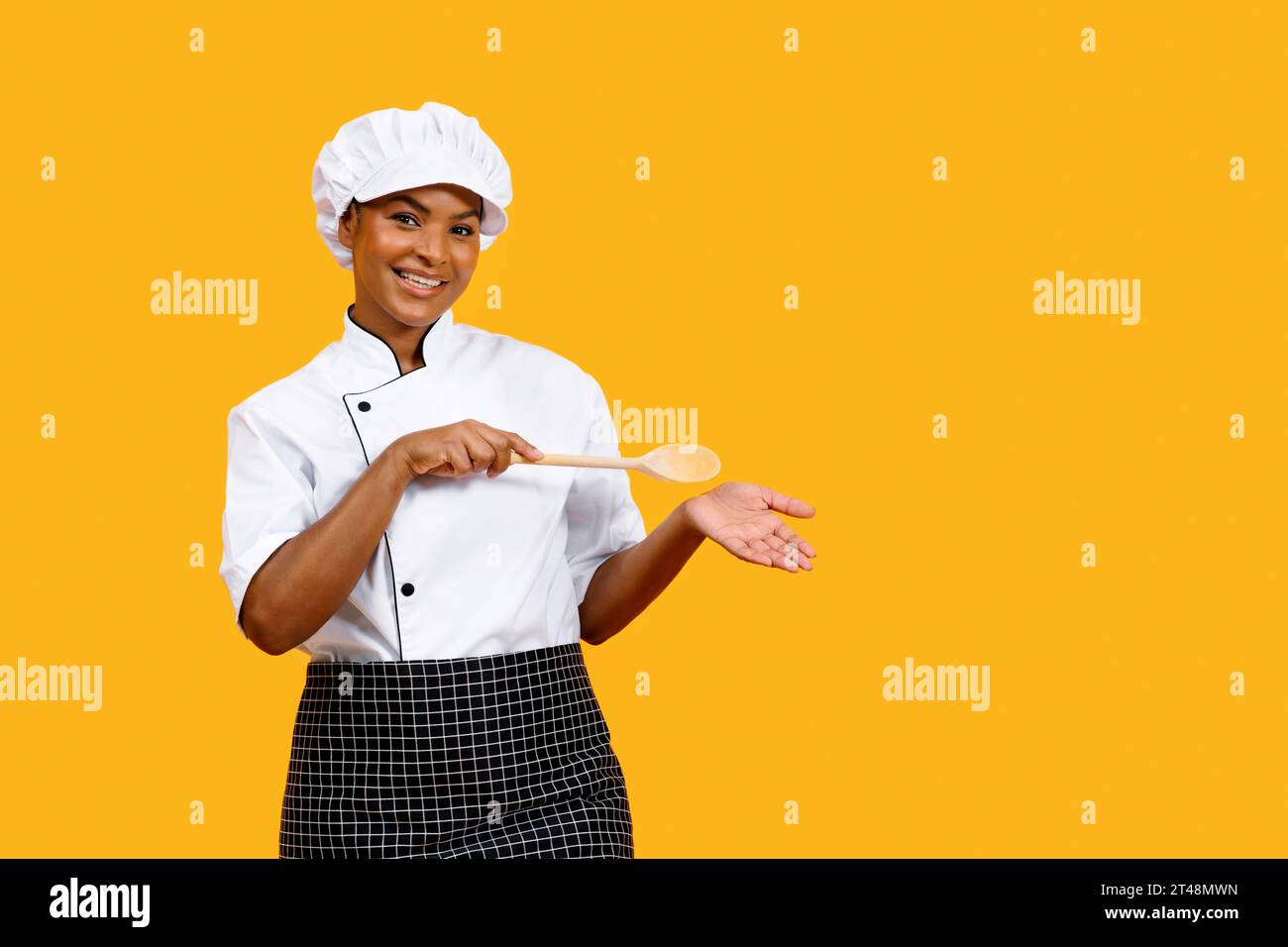 Souriant Black Chef Femme avec spatule en bois pointant vers sa paume vide Banque D'Images