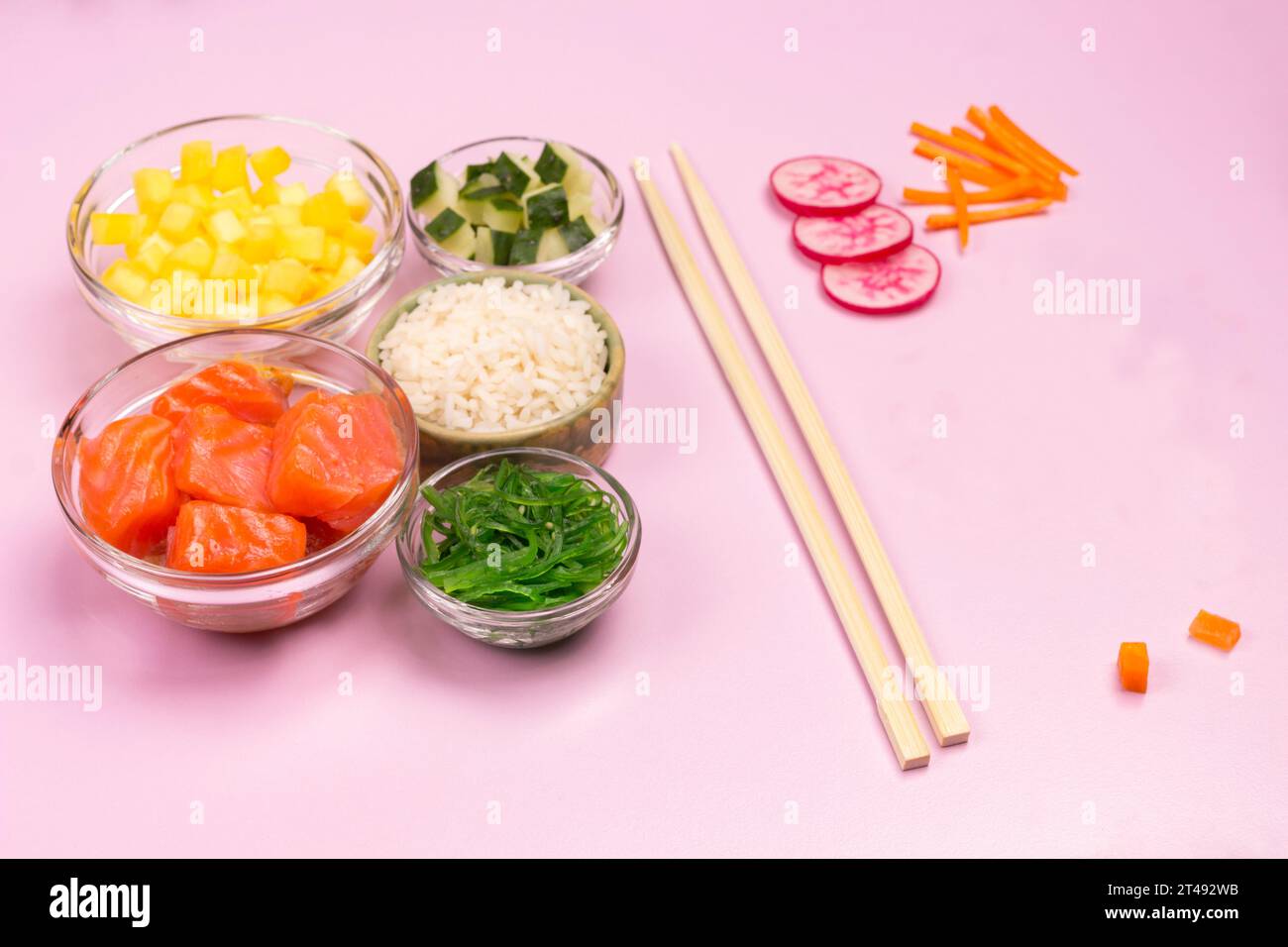 Ensemble de légumes crus, poisson rouge, riz, sauce soja dans des bols en verre. Plat hawaïen. Baguettes de bambou sur fond rose. Vue de dessus Banque D'Images