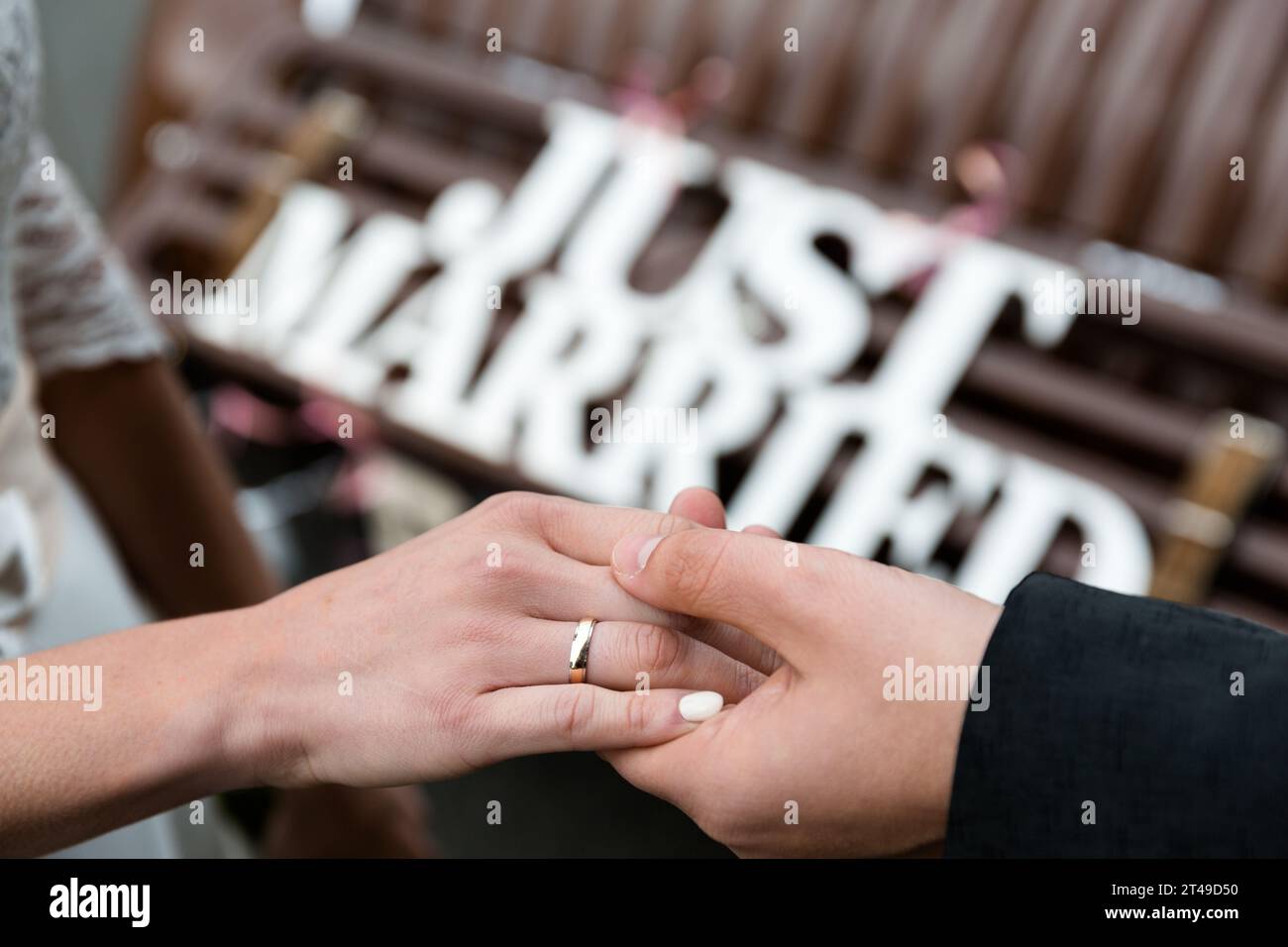 Les mains d'un couple de jeunes MARIÉS avec des anneaux, avec un signe flou "JUST MARRIED". Gros plan, capturant l'émotion et la célébration. Banque D'Images