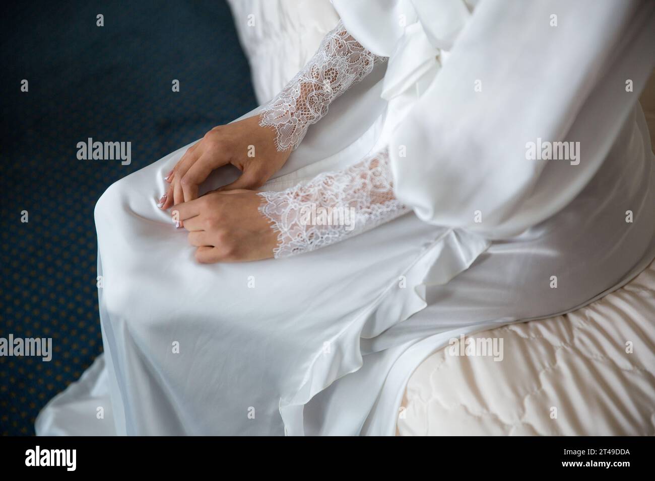 Gros plan des mains de la mariée avec des manches en dentelle, mettant en valeur l'élégance et l'anticipation sur un fond à motifs. Banque D'Images