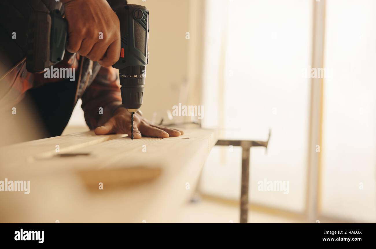 Charpentier qualifié utilise un pistolet de forage pour attacher une planche de bois pendant un projet d'amélioration de la maison. L'entrepreneur se concentre sur le travail de garniture de cuisine, ensuri Banque D'Images