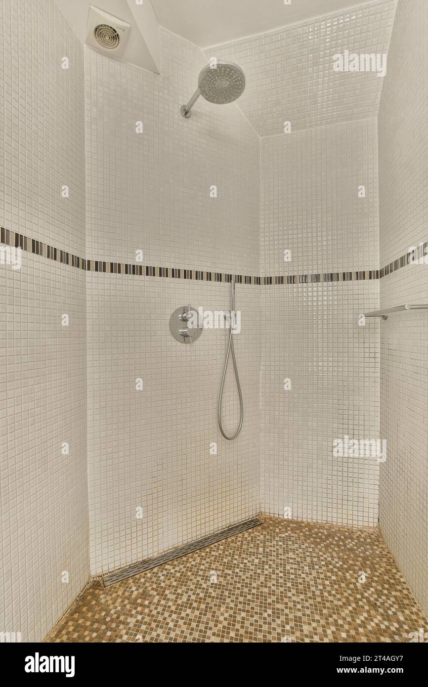 une douche carrelée blanche avec des carreaux de mosaïque bruns et noirs sur les murs, et un banc en bois dans le coin Banque D'Images