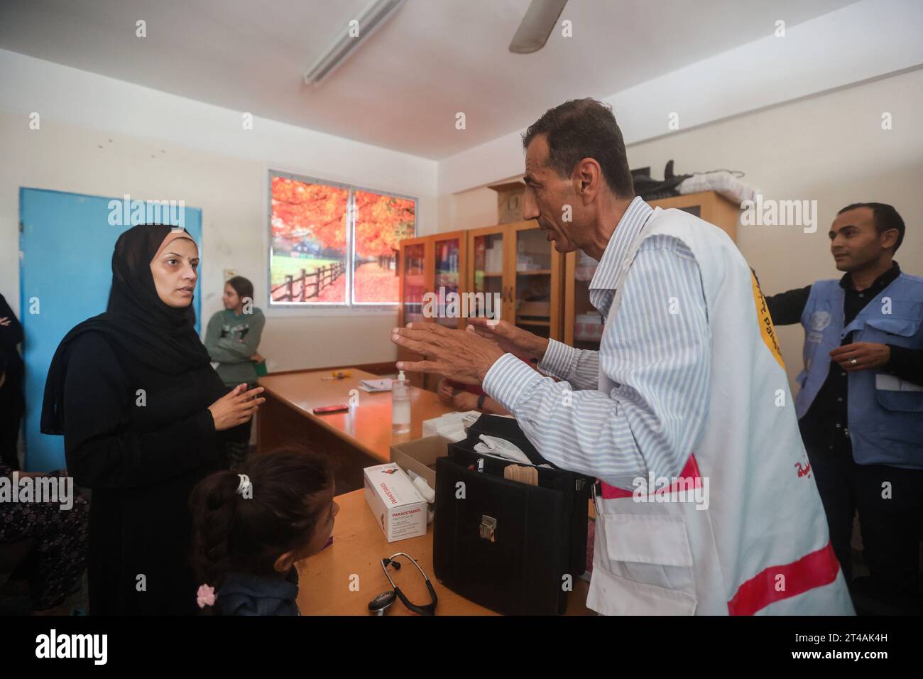 Le Dr Hassan Zein Al-DIN fournit des conseils médicaux à une palestinienne déplacée dans une école des Nations Unies pour soigner les personnes déplacées de la guerre dans le camp de Bureij, dans le centre de la bande de Gaza. Palestinien Dr Hassan Zein al-DIN, 54 ans, spécialiste de la médecine générale et des maladies chroniques. Il a été déplacé de la ville de Gaza vers la région de Bureij en raison de la guerre. Il se déplace à vélo entre les centres d’accueil pour soigner les déplacés et assurer le suivi de leurs cas au quotidien. Il se rend dans la ville de Gaza pour suivre les cas d’un certain nombre de patients dans les centres d’hébergement laissés par l’UNR Banque D'Images