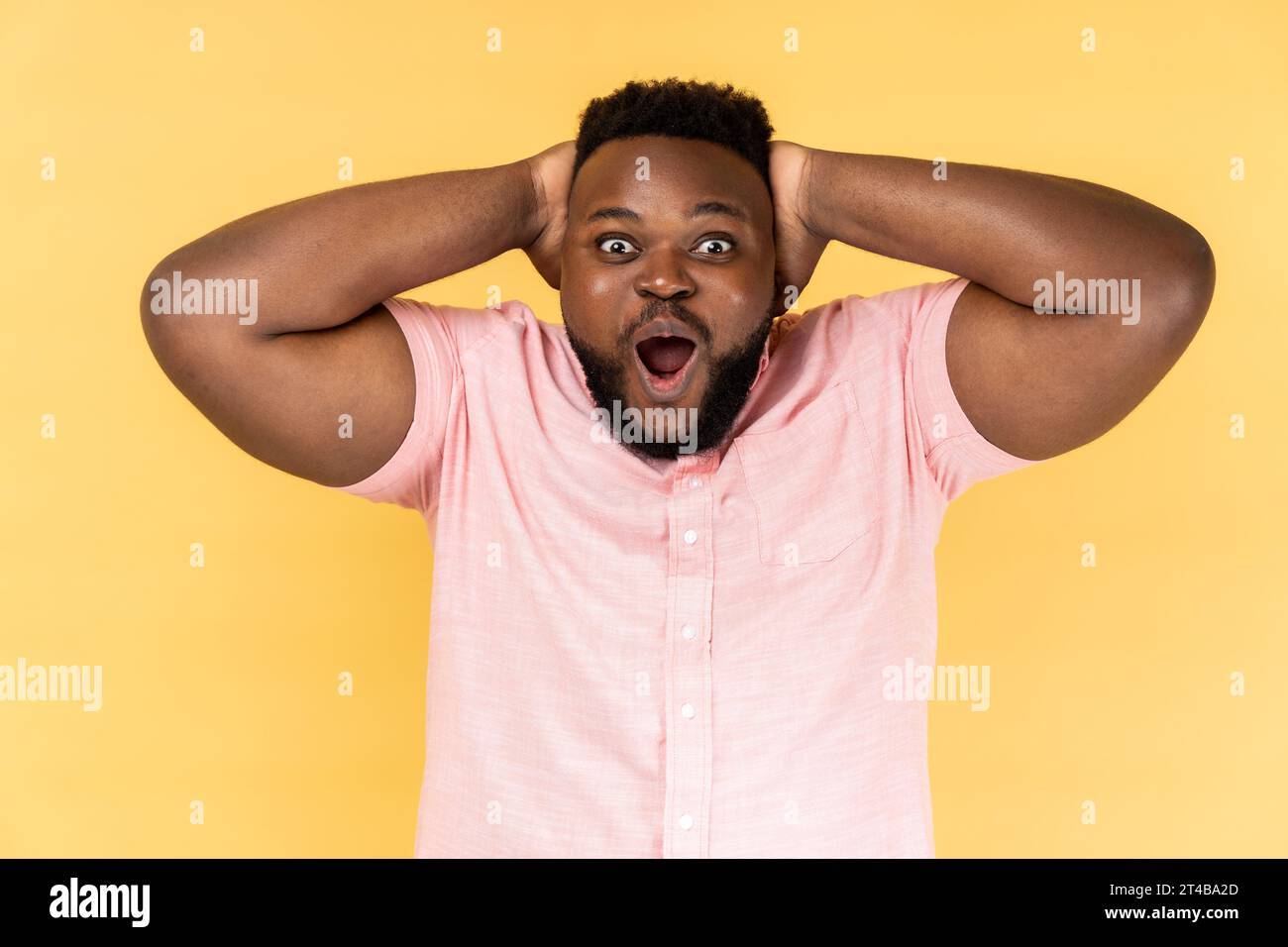 Génial. Portrait d'homme portant une chemise rose regardant la caméra avec la bouche grande ouverte, exprimant le choc et l'excitation au sujet des grandes nouvelles. Studio intérieur tourné isolé sur fond jaune. Banque D'Images