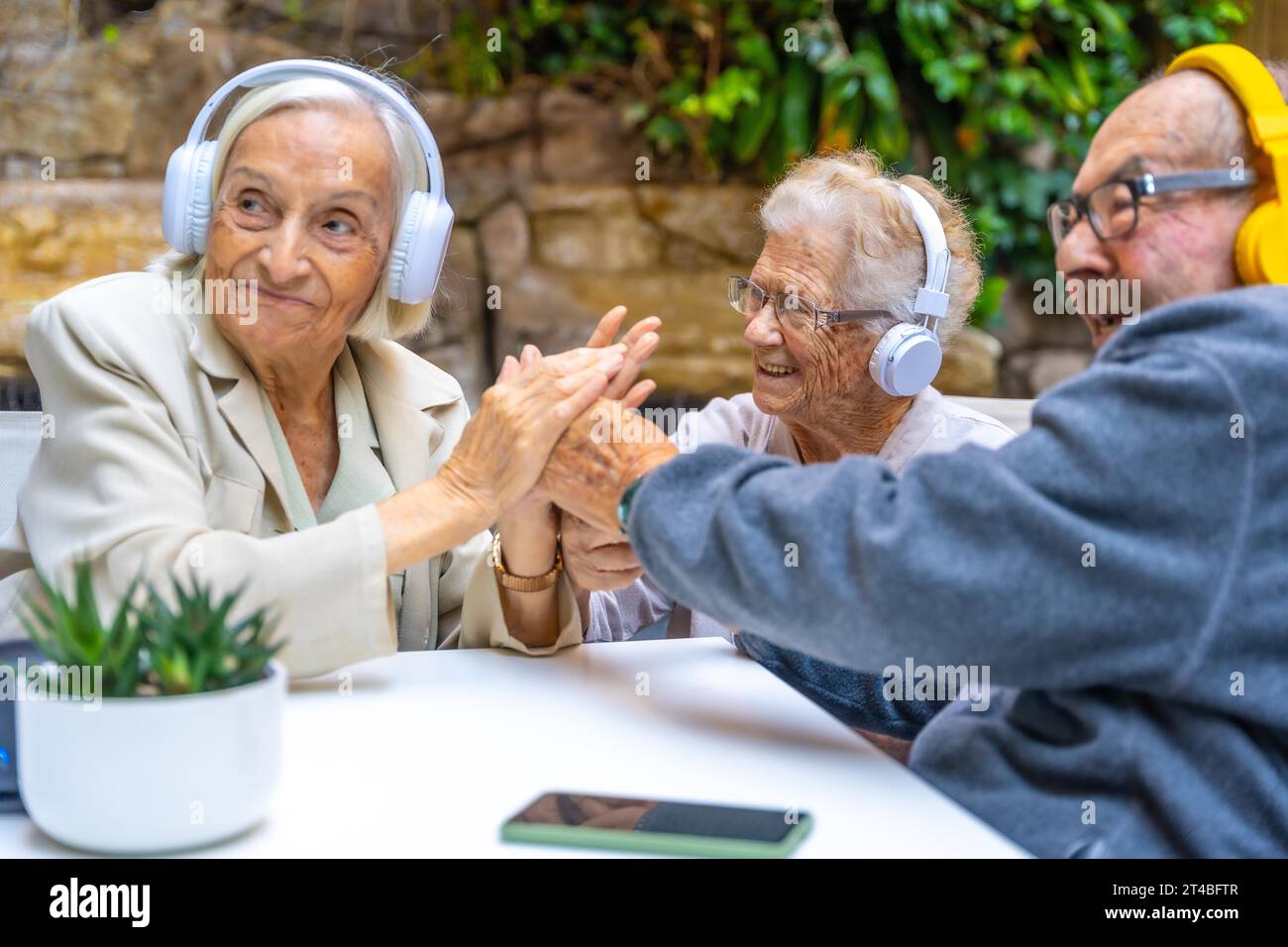 Les aînés profitent de la musique à l'aide d'écouteurs assis dans un jardin dans une maison de soins infirmiers Banque D'Images