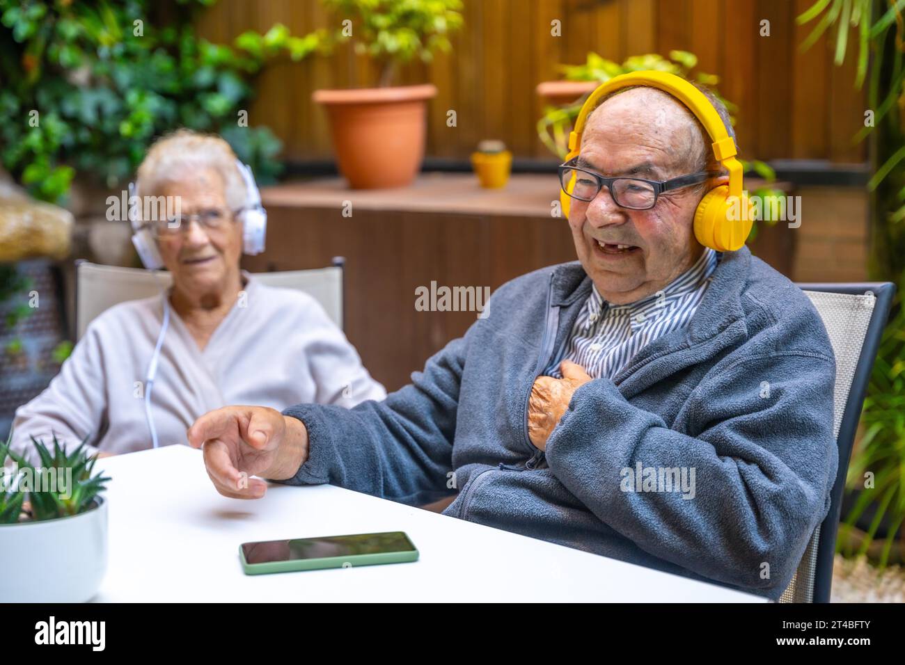 Heureux vieil homme écoutant de la musique avec des écouteurs dans un gériatrique à côté d'autres personnes âgées Banque D'Images