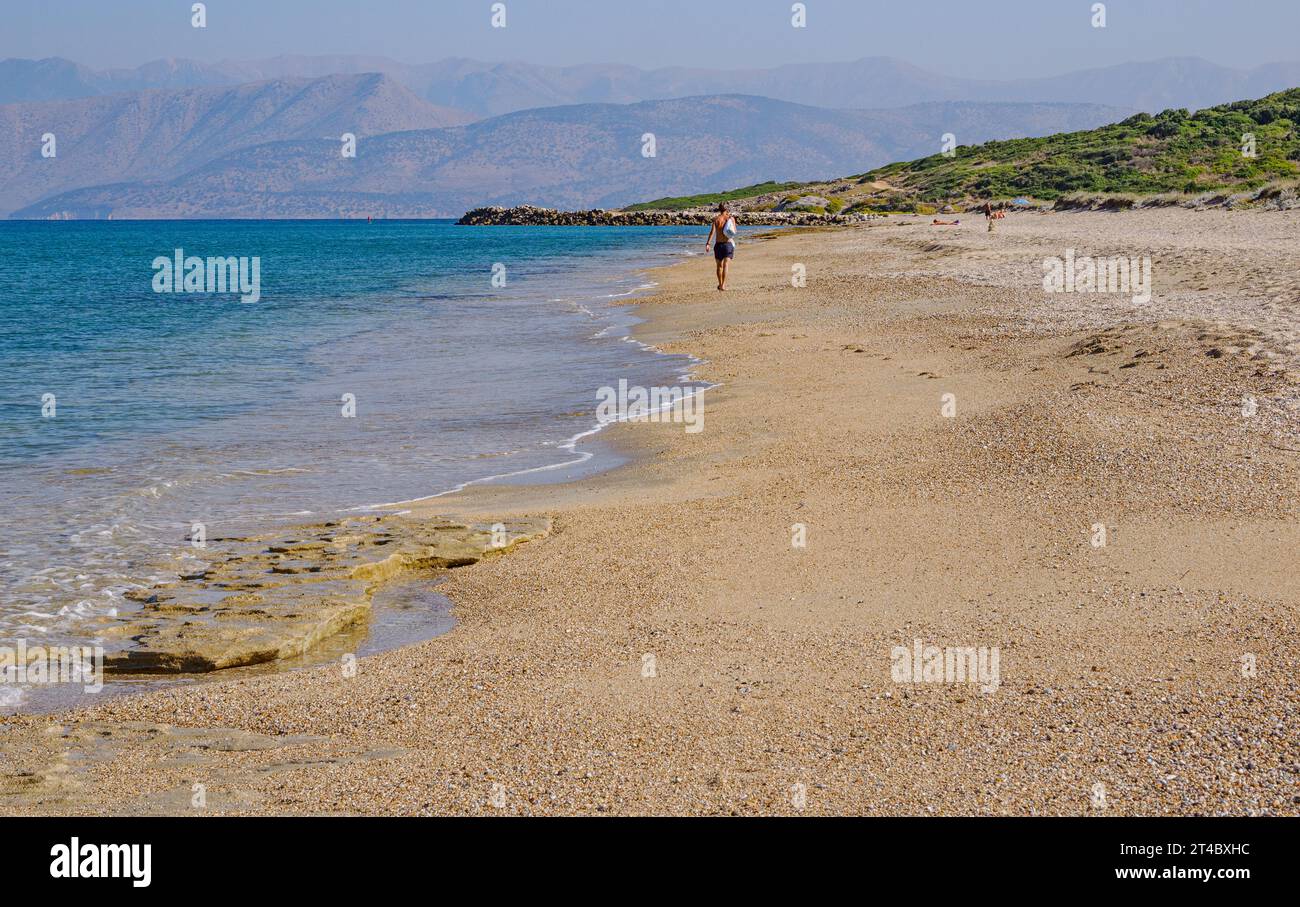 Homme marchant le long de la plage d'Almiros vers le cap Agia Ekatarinis sur la côte nord de Corfou avec les montagnes lointaines de l'Albanie - Îles Ioniennes Grèce Banque D'Images