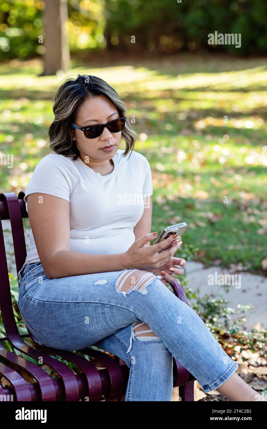 Image verticale d'une femme portant des lunettes de soleil, regardant son téléphone Banque D'Images