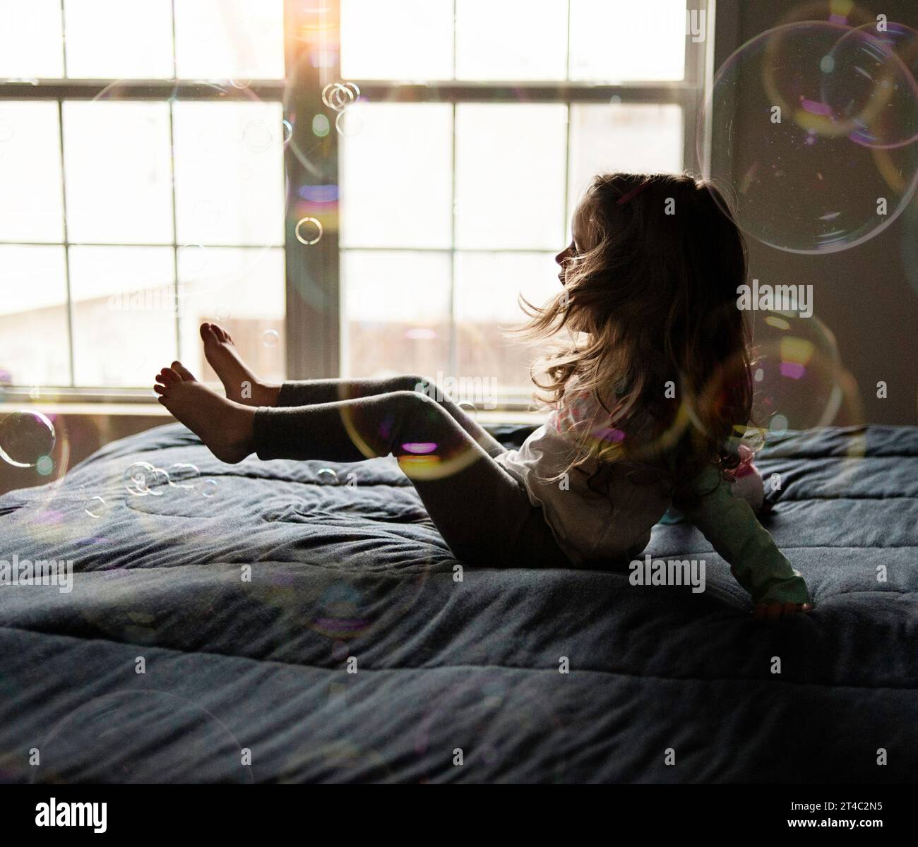 Petite fille rebondissant sur le lit avec des bulles Banque D'Images