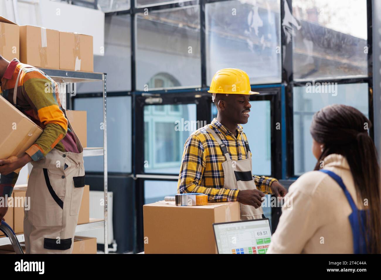 Le groupe de travailleurs d'entrepôt vérifie le ticket de cueillette et prépare le colis pour l'expédition. Tous les employés de Black Storehouse discutent en équipe tout en gérant la préparation des commandes des clients dans la salle de stockage Banque D'Images