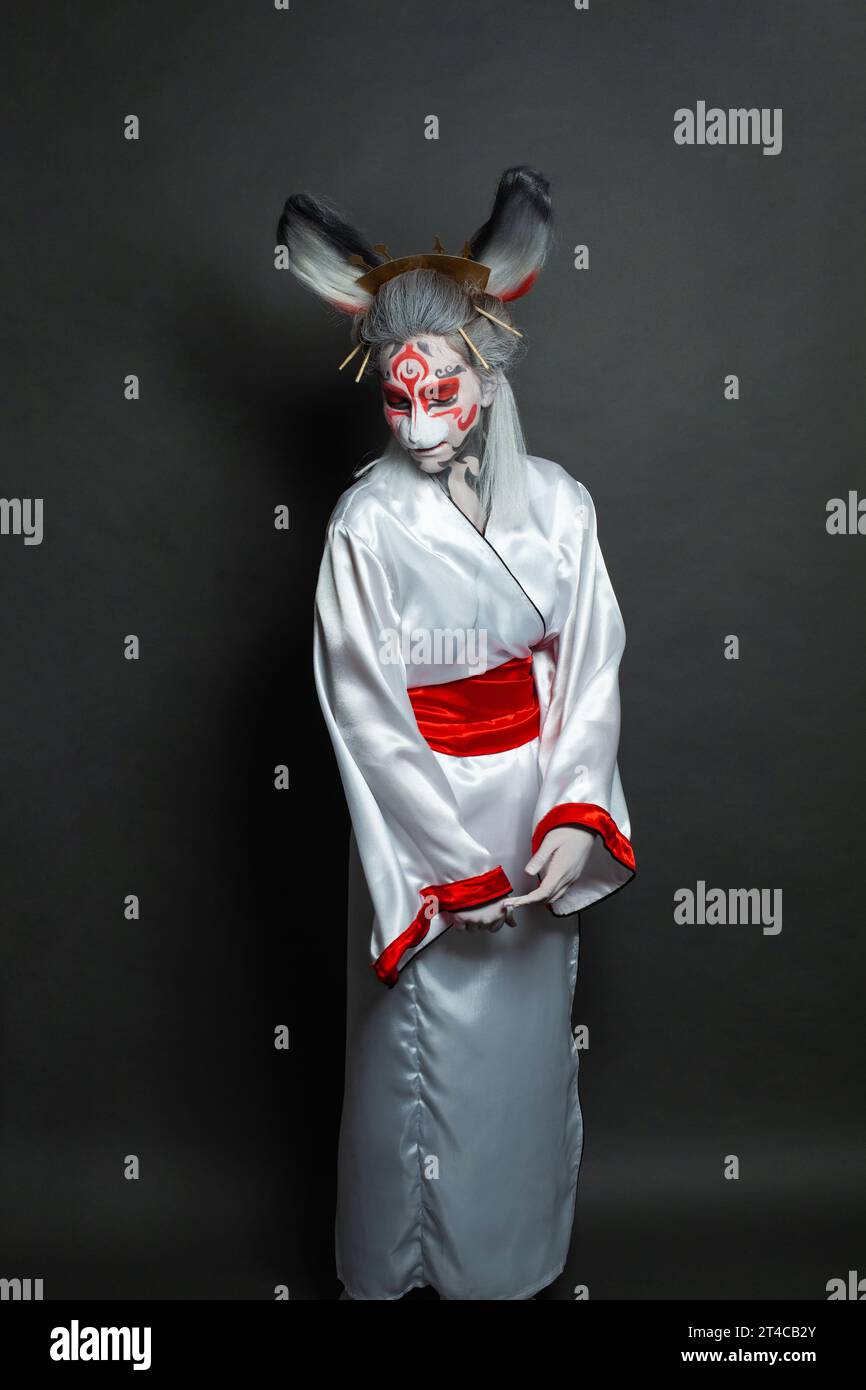 Jeune femme avec maquillage animal, masque et costume asiatique de scène debout sur fond noir. Halloween, carnaval, performance et concept de théâtre Banque D'Images