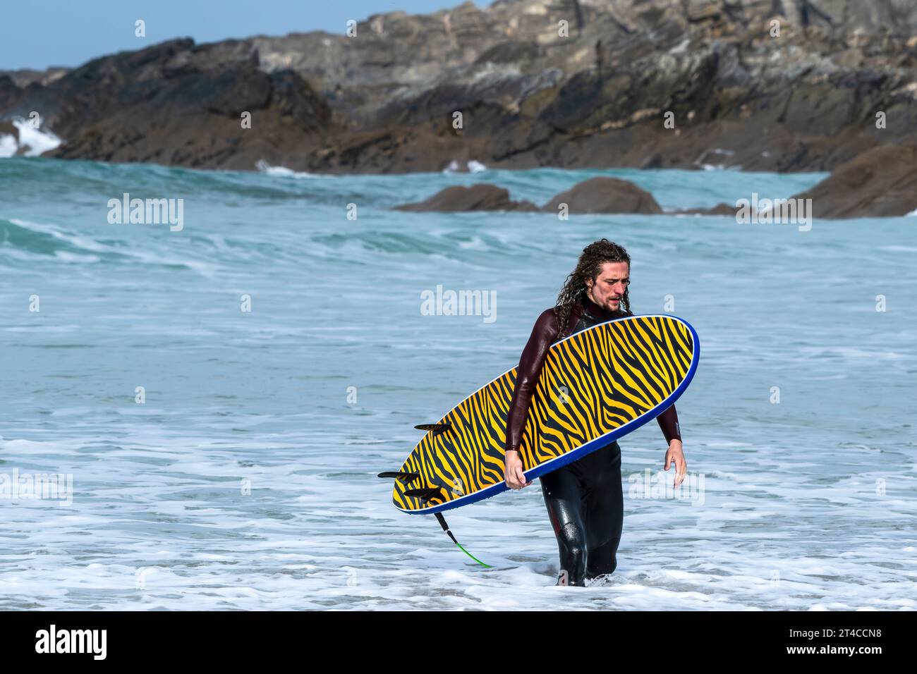 Un surfeur portant sa planche de surf distinctive après une session de surf à Fistral à Newquay en Cornouailles au Royaume-Uni. Banque D'Images