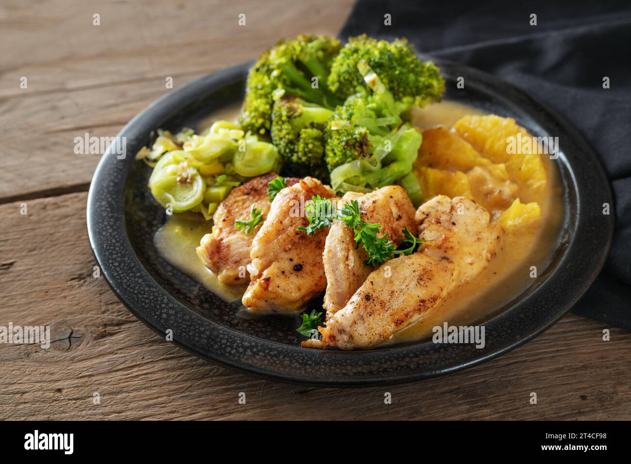 Filet de poulet en sauce orange avec légumes poireaux brocoli sur une assiette noire sur bois rustique foncé, plat de régime pauvre en glucides, espace de copie, foyer sélectionné, nar Banque D'Images