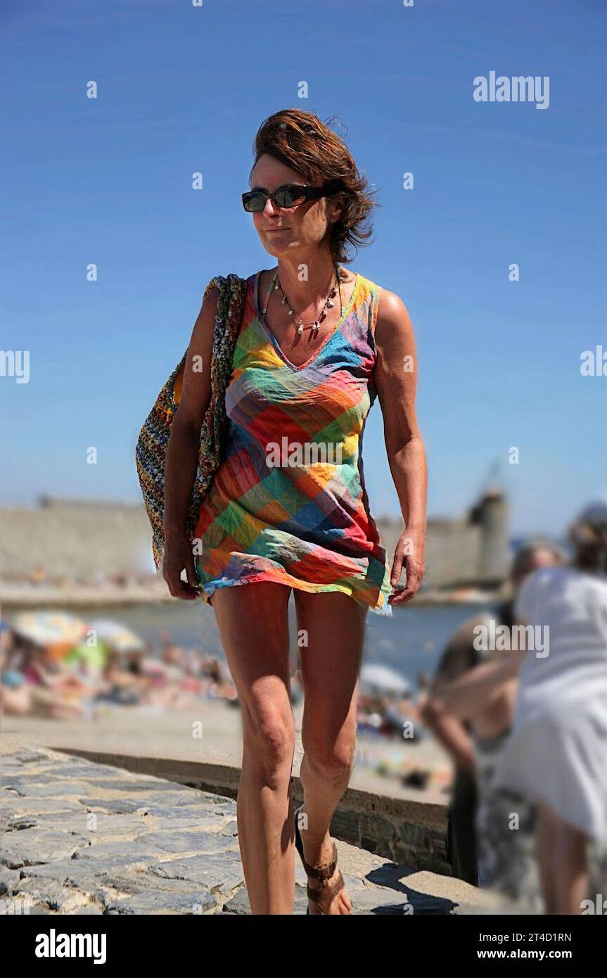 Séduisante jeune femme brune dans une mini-robe aux couleurs vives à Plage St-Vincent, Collioure, Pyrénées-Orientales, Languedoc-Roussillon, France. MODÈLE VALIDÉ Banque D'Images