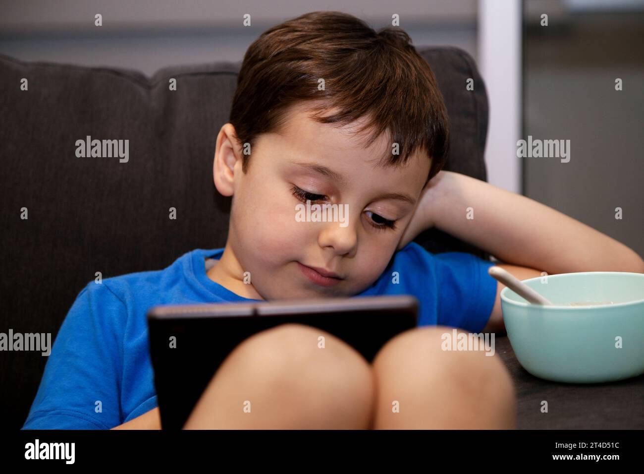 Un garçon assis sur un canapé à la maison jouant avec une tablette. Expression sérieuse sur son visage. Conception de l'addiction aux jeux électroniques chez le jeune enfant. Banque D'Images