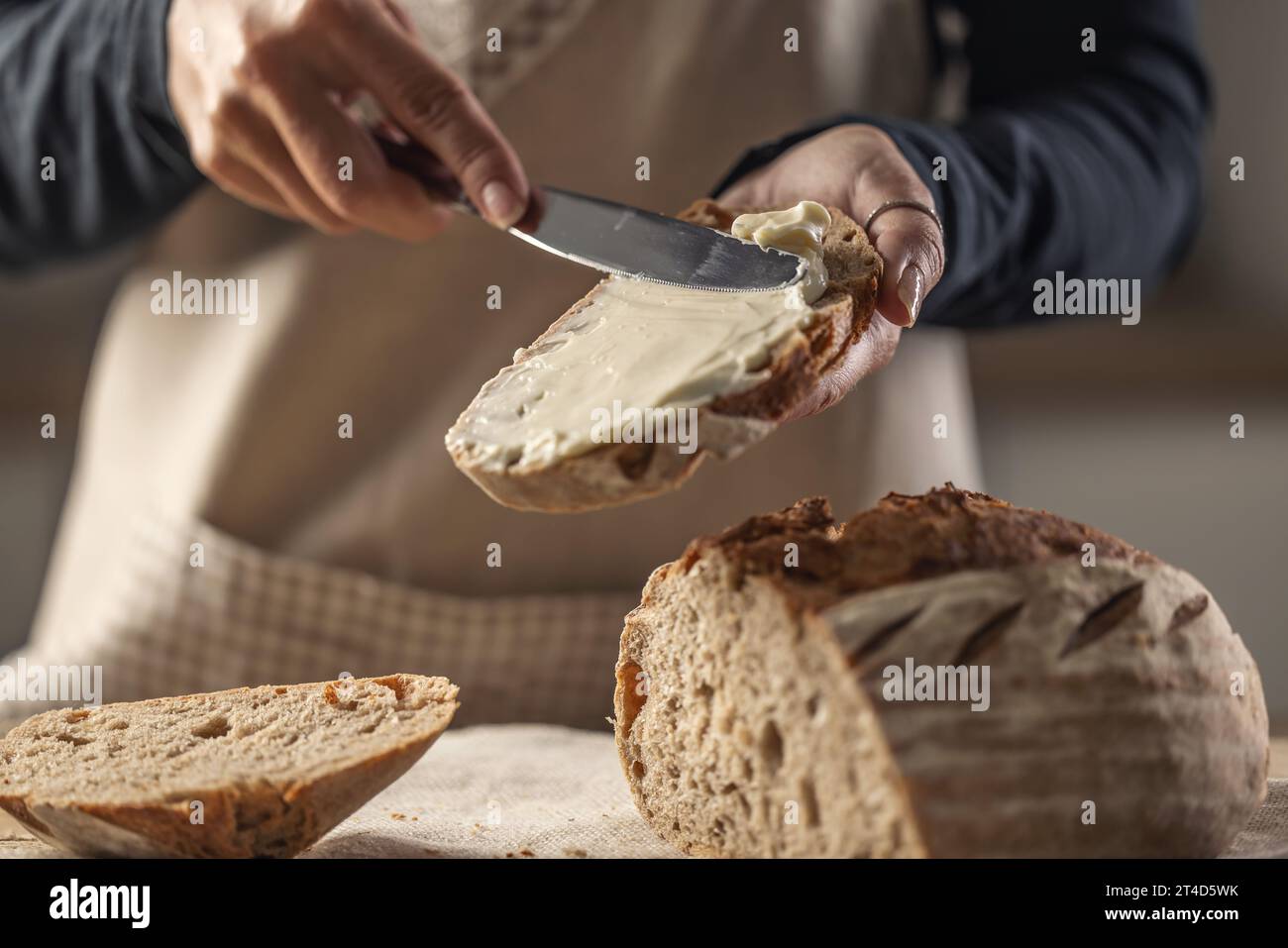 Une femme fait du pain délicieux, étale du fromage à la crème avec un couteau à couverts - Close up. Mains de femme étalant le fromage à la crème sur la tranche de pain. Banque D'Images