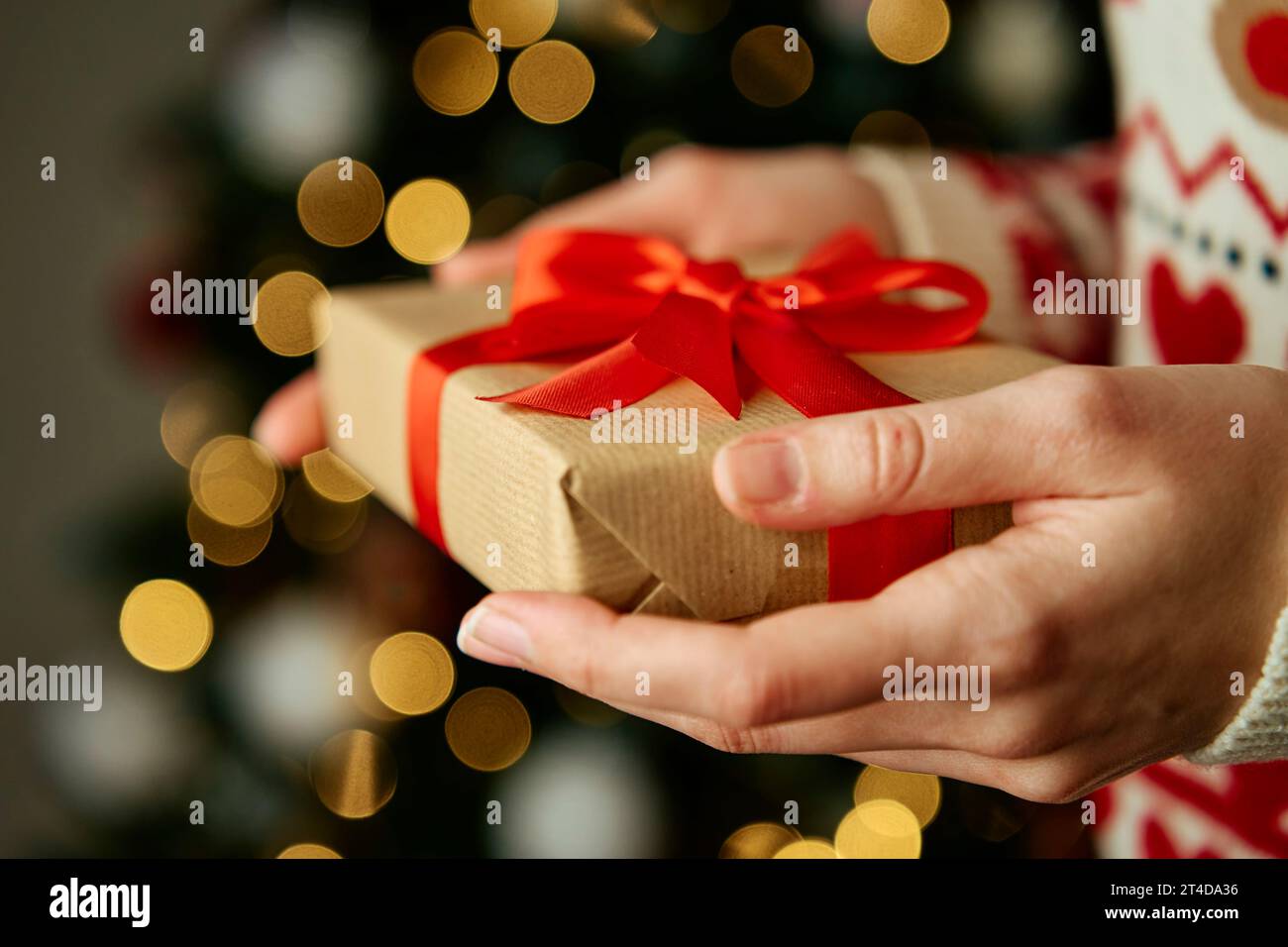 Femme en chandail chaud tenant une boîte cadeau emballage en papier artisanal avec ruban de fête. Cadeau pour les vacances d'hiver. Noël et bonne fête du nouvel an Banque D'Images