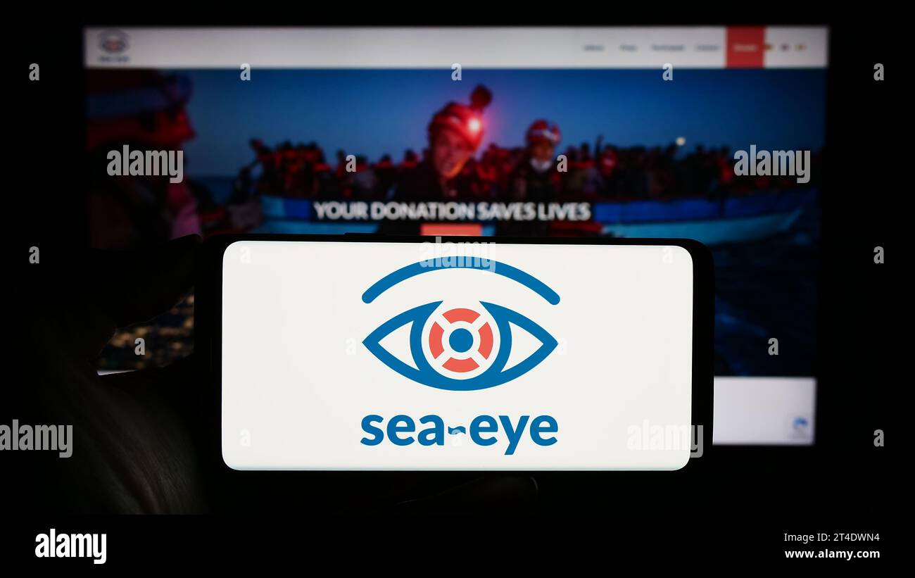 Personne détenant un téléphone portable portant le logo de l'association allemande de sauvetage en mer Sea-Eye e.V. devant la page web. Concentrez-vous sur l'affichage du téléphone. Banque D'Images