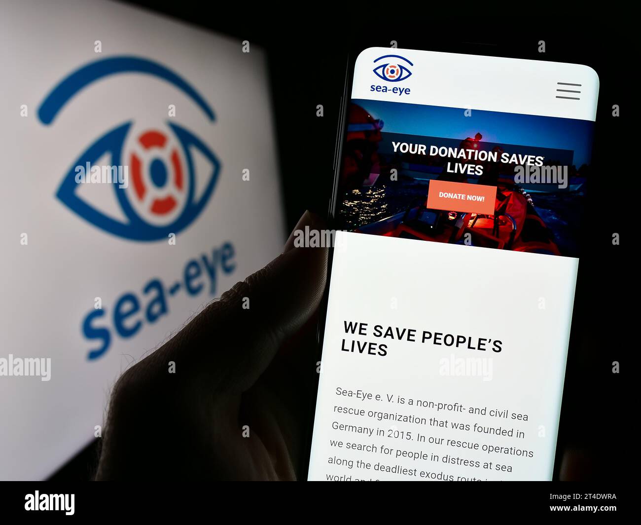 Personne détenant un téléphone portable avec la page web de l'association allemande de sauvetage en mer Sea-Eye e.V. devant le logo. Concentrez-vous sur le centre de l'écran du téléphone. Banque D'Images