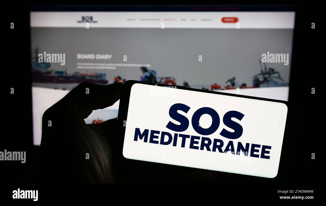 Personne détenant un téléphone portable avec le logo de l'organisation française de sauvetage en mer SOS Mediterranee devant la page web. Concentrez-vous sur l'affichage du téléphone. Banque D'Images