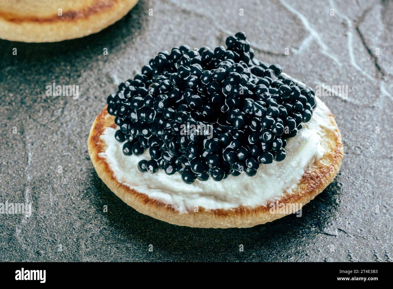 Un blini au caviar et au fromage à la crème, un gros plan sur un fond d'ardoise noire Banque D'Images