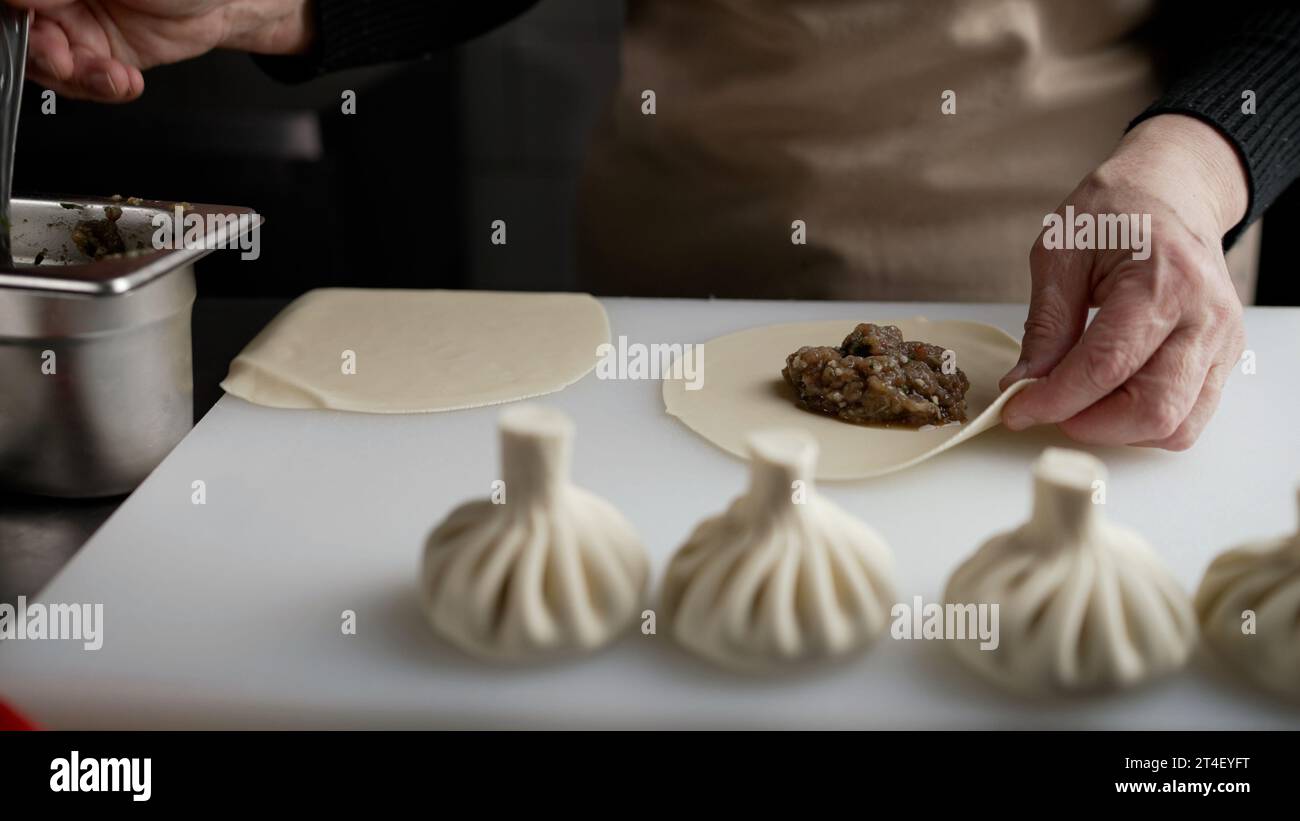 Les mains des femmes font des manti, des khinkali, des boulettes de pâte avec une garniture à la viande. Nourriture maison. Gros plan d'un chef préparant de la pâte avec de la viande hachée. Mains Banque D'Images
