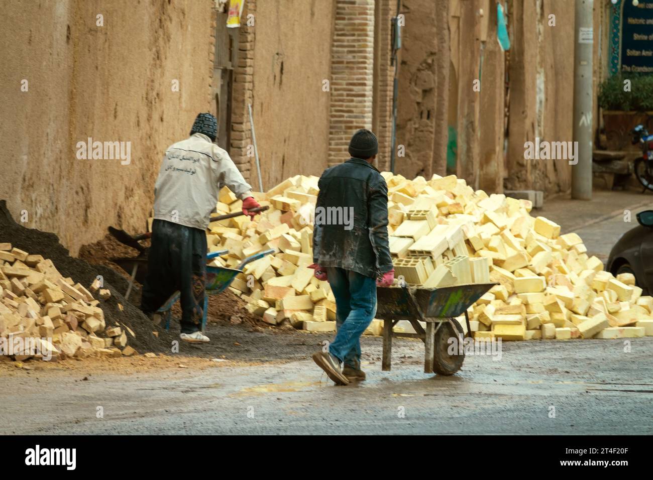 Kashan, Iran - 24 décembre 2022 : Construction d'une maison en briques. Montagne de briques et de sable, ouvrier de construction avec une brouette Banque D'Images