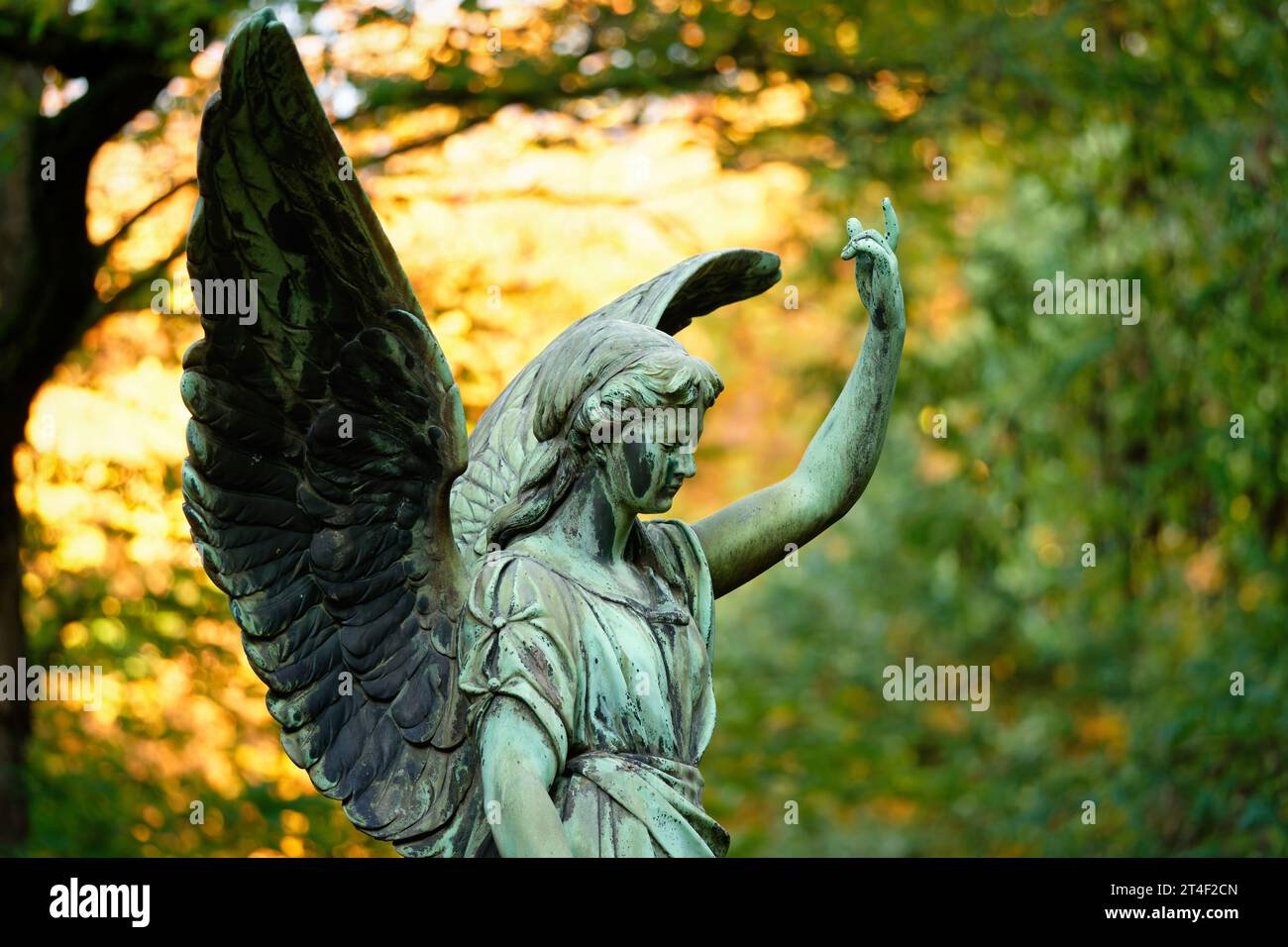 un ange aux ailes dans un cimetière devant des feuilles d'automne lumineuses en arrière-plan lève un bras vers le ciel Banque D'Images