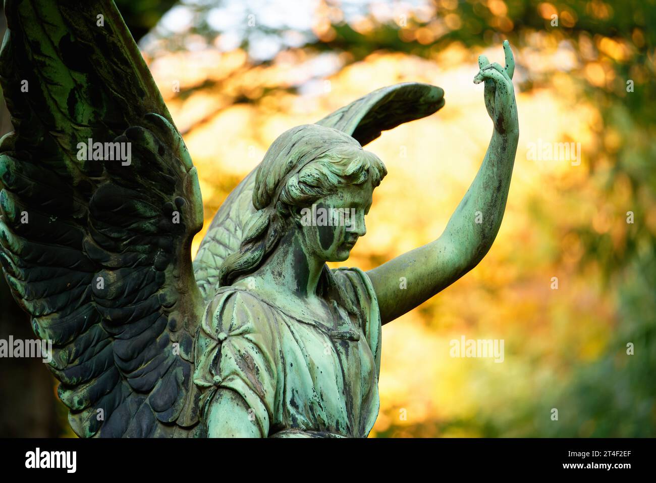 un ange aux ailes dans un cimetière devant des feuilles d'automne lumineuses en arrière-plan lève un bras vers le ciel Banque D'Images