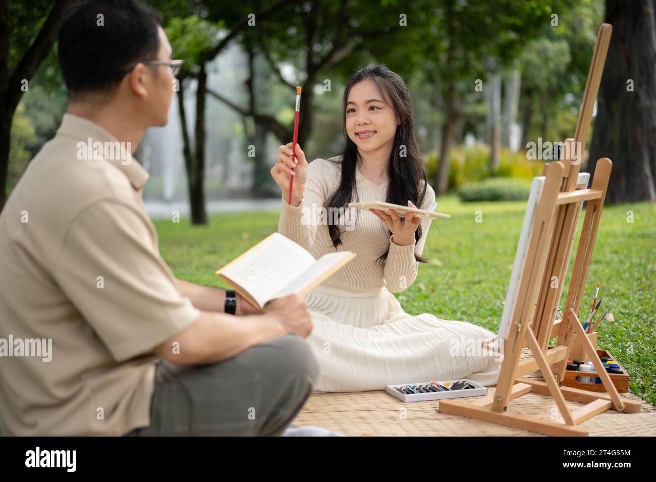 Une jeune fille asiatique joyeuse et charmante aime peindre avec son père dans un parc verdoyant, pique-niquer et passer du temps heureux ensemble. Banque D'Images