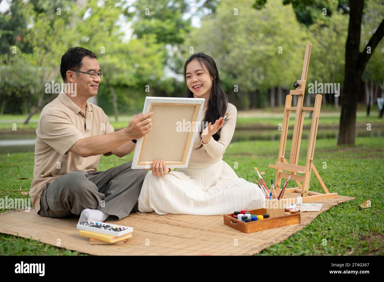 Une fille asiatique charmante et joyeuse aime pique-niquer dans un parc verdoyant avec son père, passer du temps à créer et peindre une image sur une toile ensemble. HAP Banque D'Images