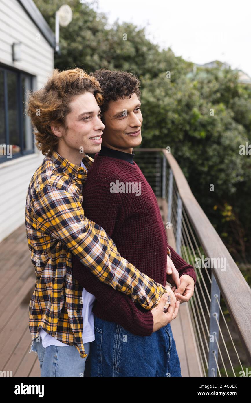 Heureux et diversifié couple masculin gay embrassant au balcon avec vue sur la forêt Banque D'Images
