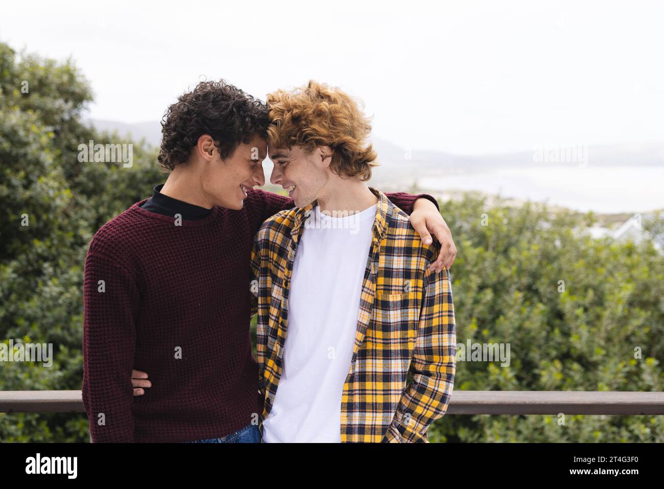 Heureux couple masculin gay diverse embrassant au balcon sur la vue de la forêt, espace de copie Banque D'Images