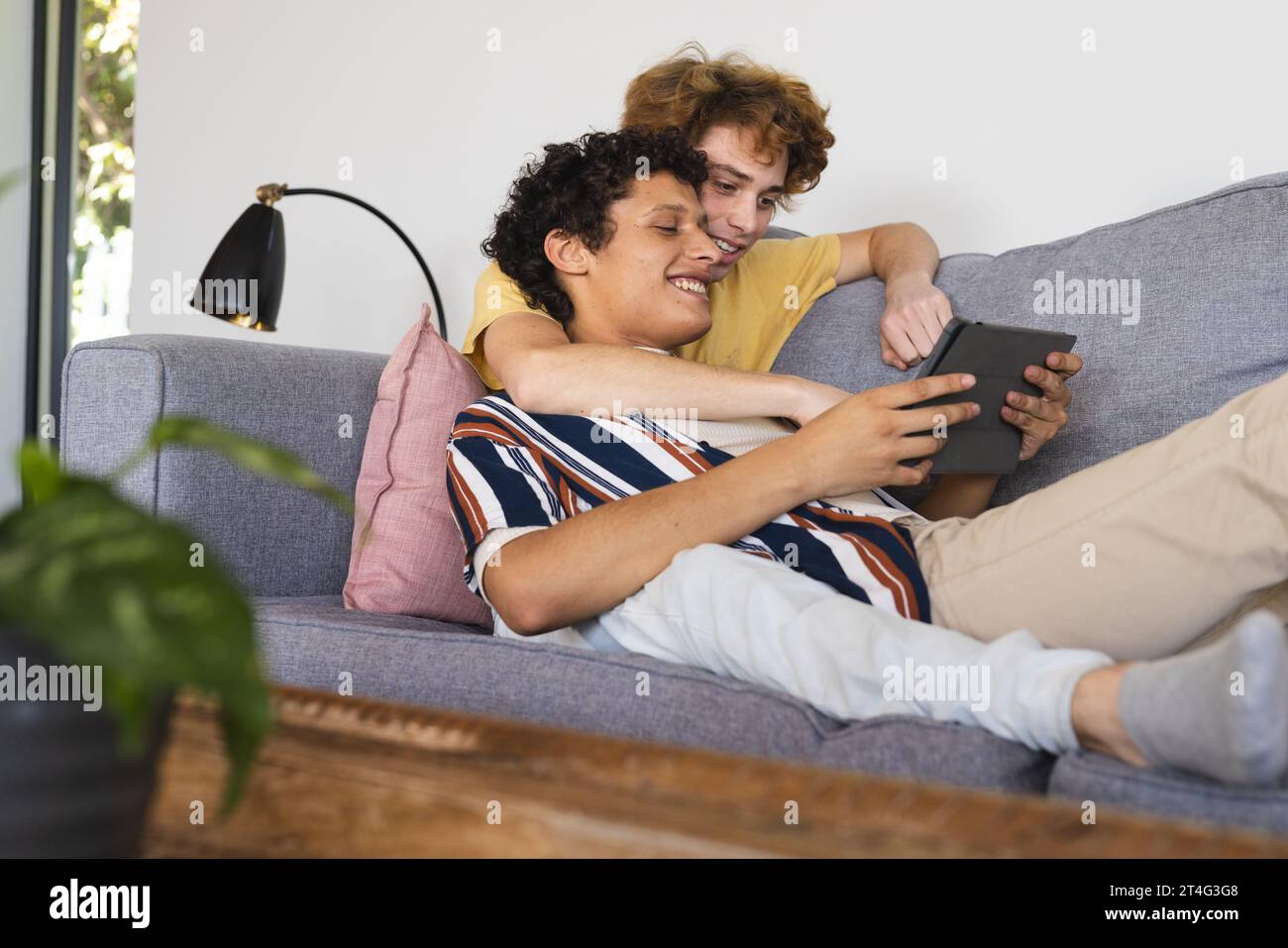 Heureux couple masculin gay diversifié utilisant la tablette et embrassant à la maison Banque D'Images