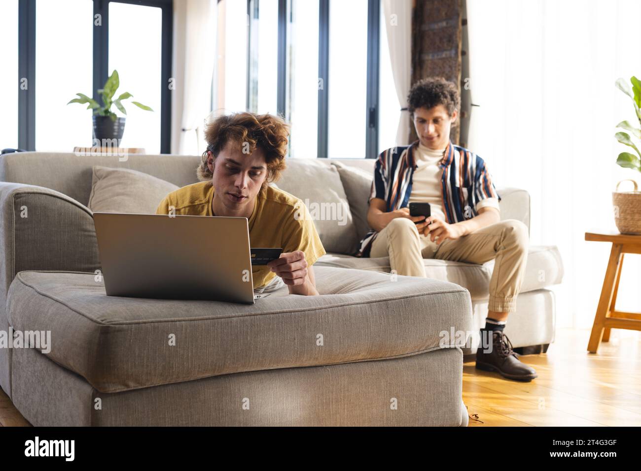 Heureux couple masculin gay diversifié utilisant un ordinateur portable et smartphone avec carte de crédit à la maison Banque D'Images