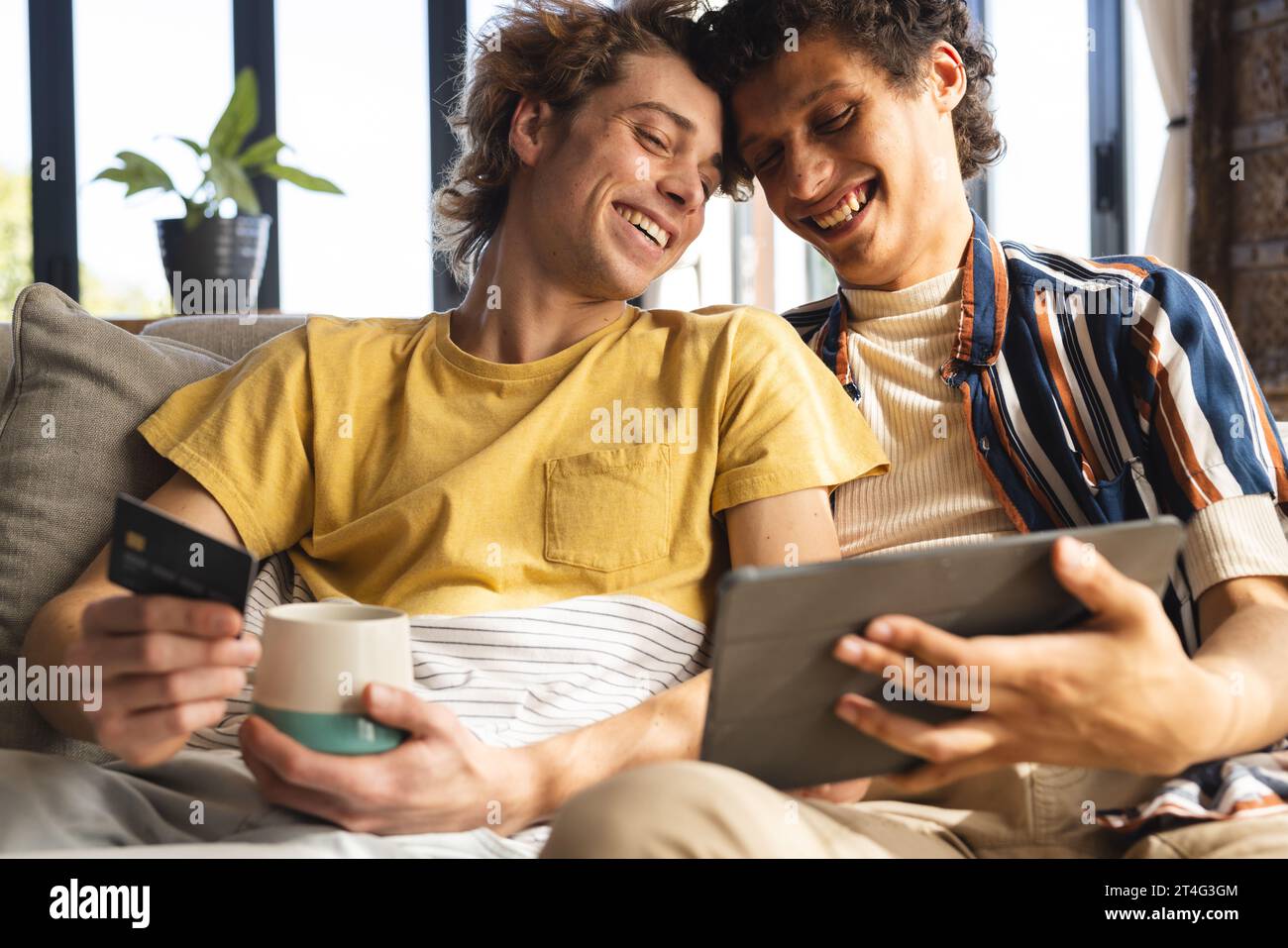 Heureux couple masculin gay diversifié utilisant tablette avec carte de crédit à la maison Banque D'Images
