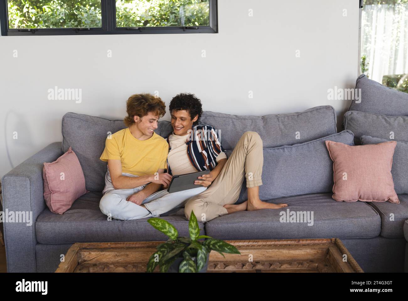 Heureux couple masculin gay diversifié utilisant la tablette et embrassant à la maison Banque D'Images