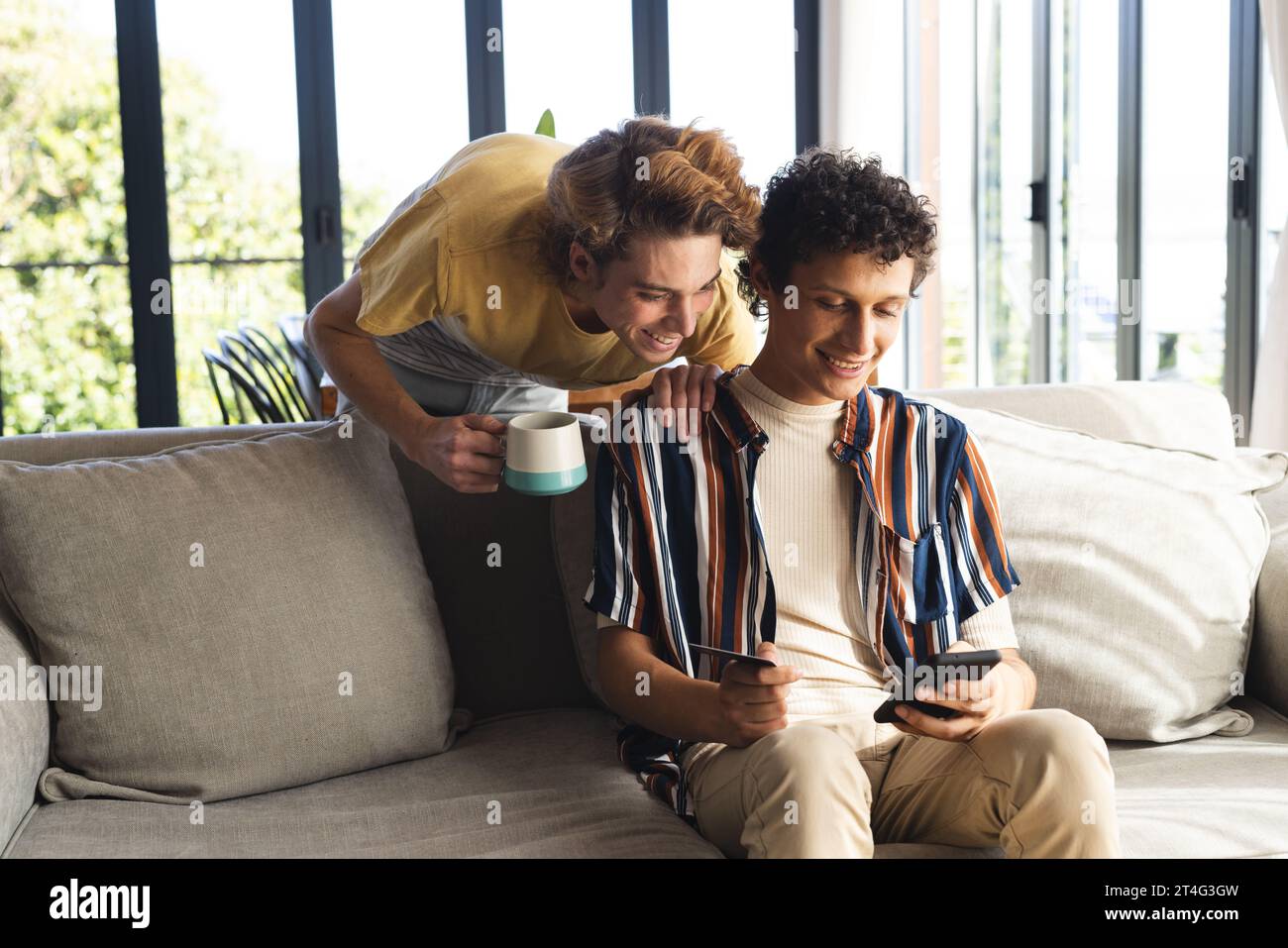 Heureux couple masculin gay diversifié utilisant smartphone avec carte de crédit à la maison Banque D'Images