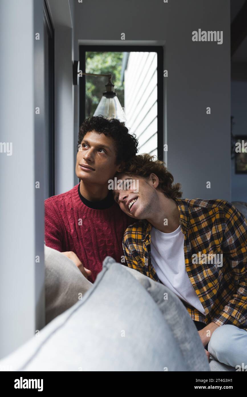 Heureux couple masculin gay diversifié embrassant et regardant par la fenêtre à la maison Banque D'Images