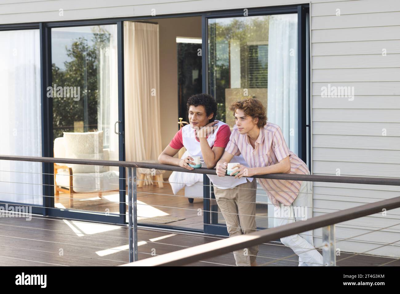 Heureux couple masculin gay diverse tenant des tasses de café au balcon Banque D'Images