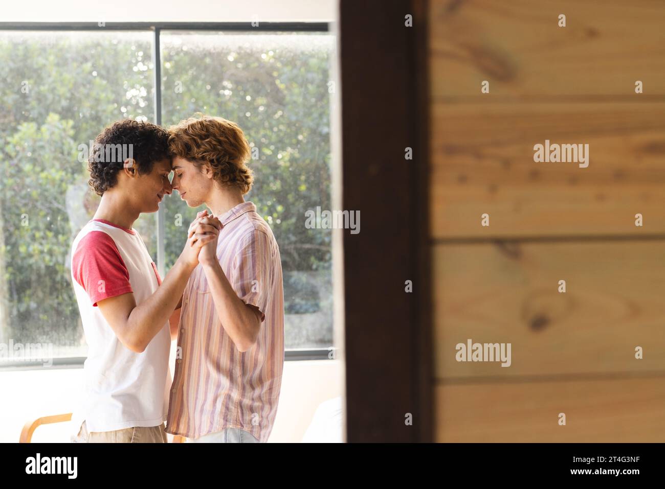 Heureux couple masculin gay diversifié avec cheveux bouclés dansant à la maison, espace de copie Banque D'Images