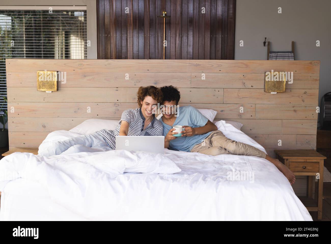 Heureux couple masculin gay diversifié couché sur le lit et utilisant un ordinateur portable à la maison Banque D'Images