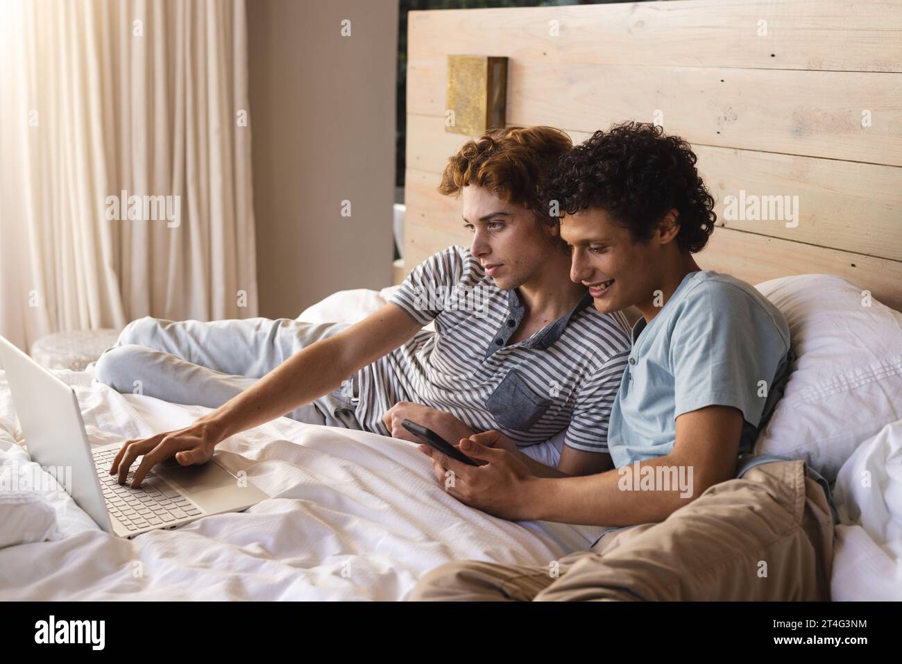 Heureux couple masculin gay diversifié couché sur le lit et utilisant un ordinateur portable à la maison Banque D'Images