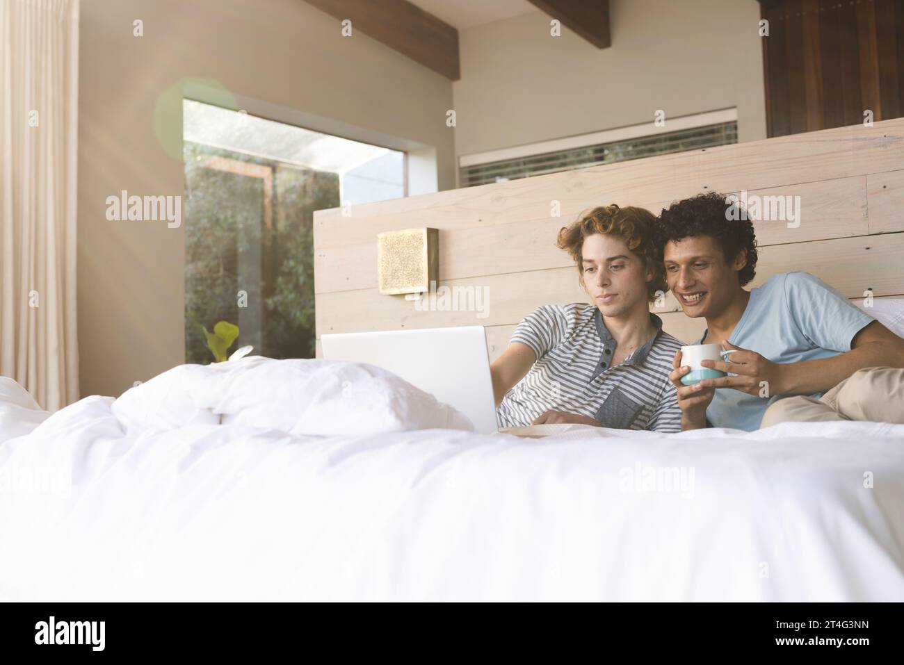 Heureux couple masculin gay diversifié couché sur le lit et utilisant un ordinateur portable à la maison Banque D'Images