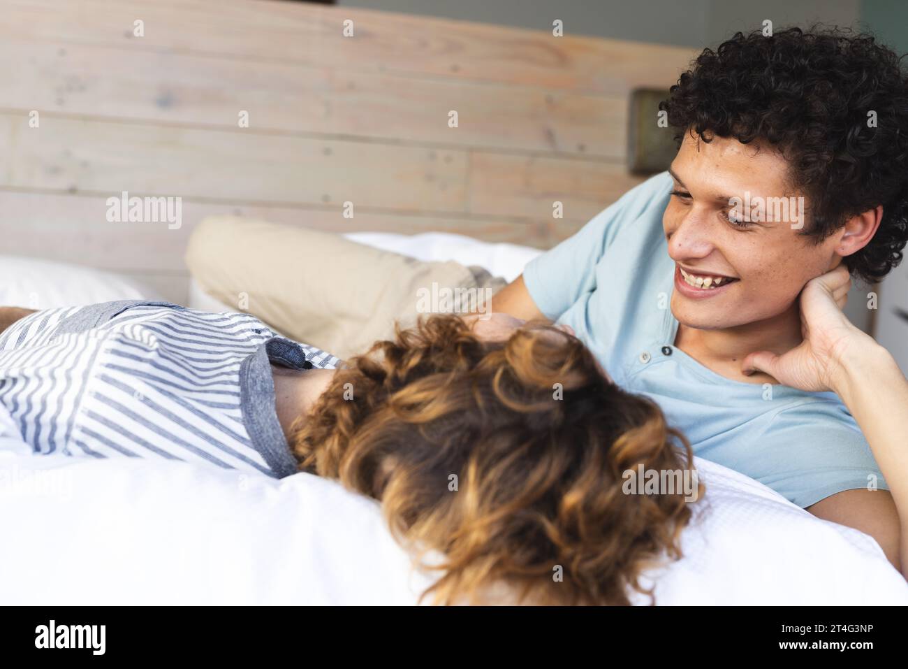 Heureux et diversifié couple masculin gay couché sur le lit et se regardant à la maison Banque D'Images