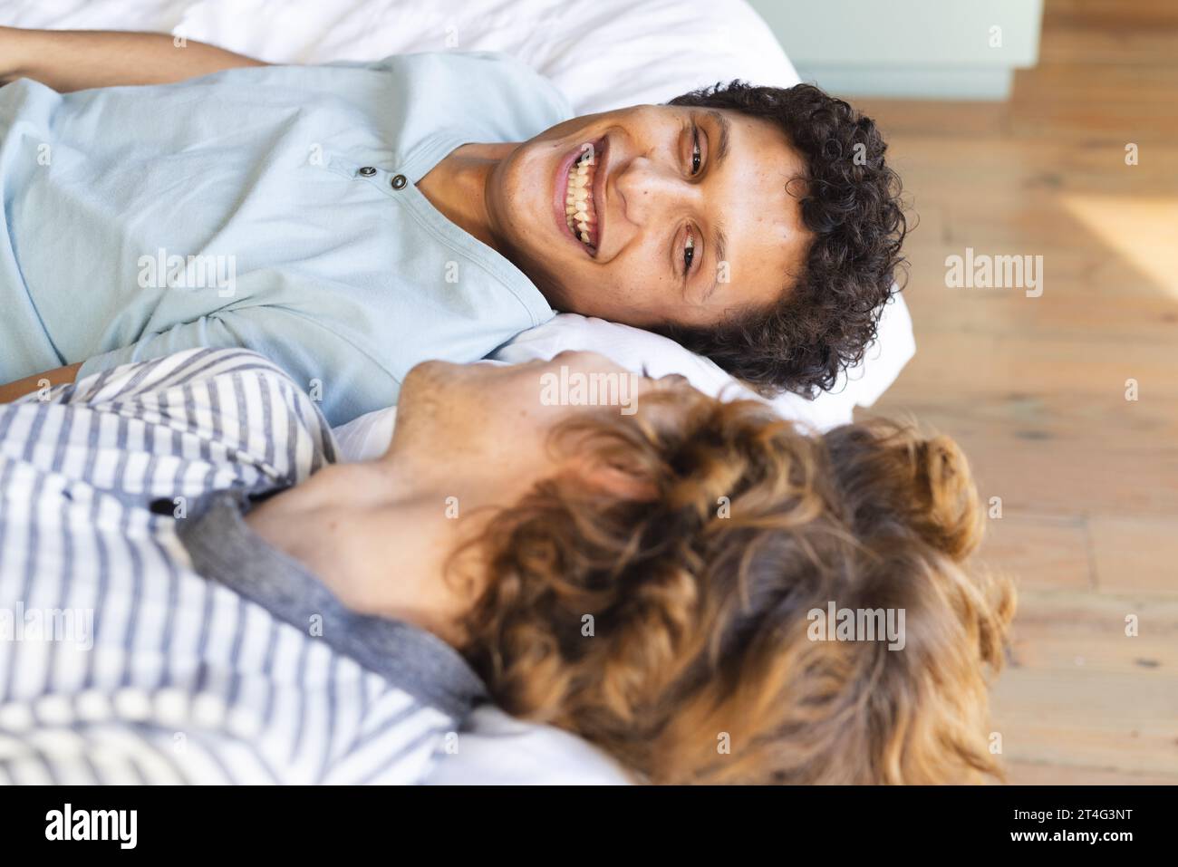 Heureux et diversifié couple masculin gay couché sur le lit et se regardant à la maison Banque D'Images