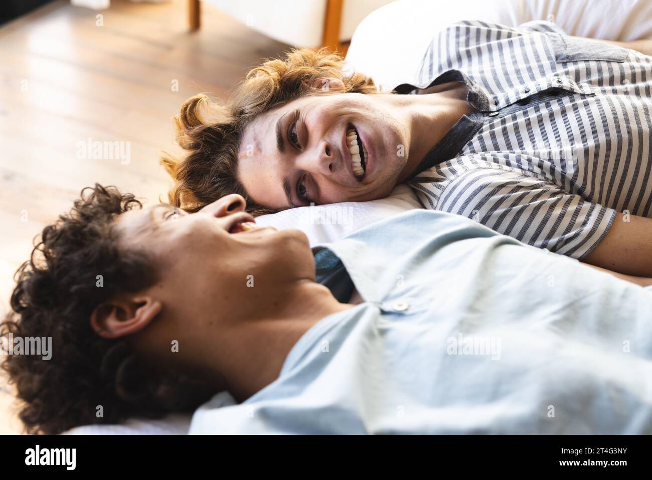 Heureux et diversifié couple masculin gay couché sur le lit et se regardant à la maison Banque D'Images