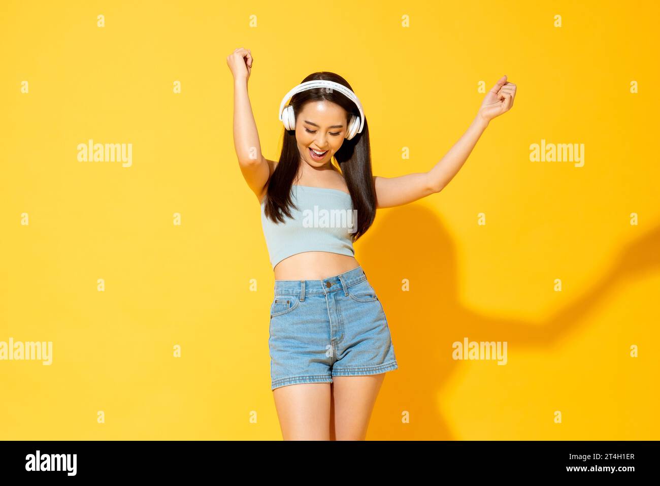 Jeune jolie femme asiatique portant des écouteurs écoutant de la musique et dansant dans le studio fond de couleur jaune Banque D'Images